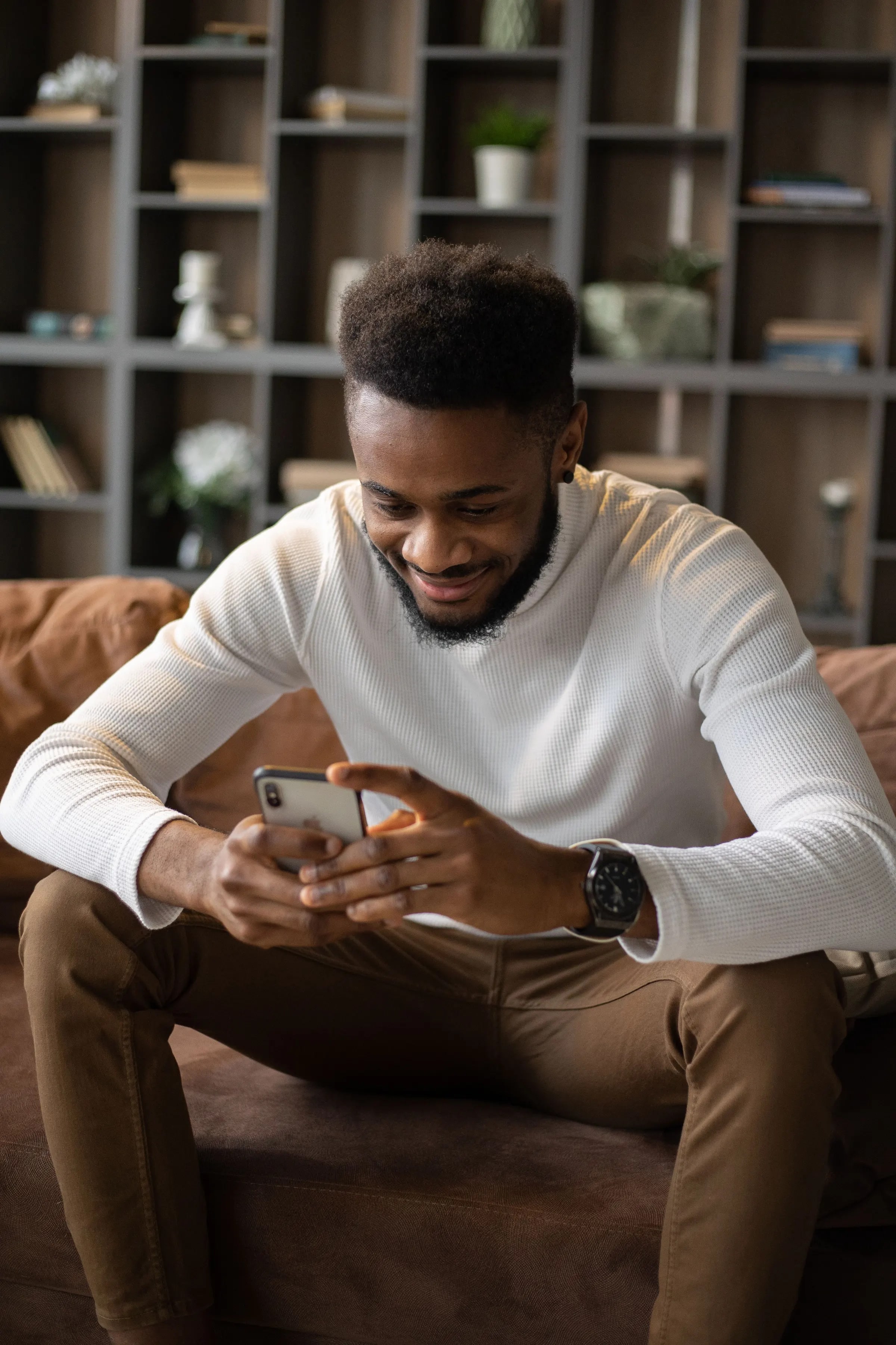 Een man zit op de bank en bekijkt iets op zijn smartphone