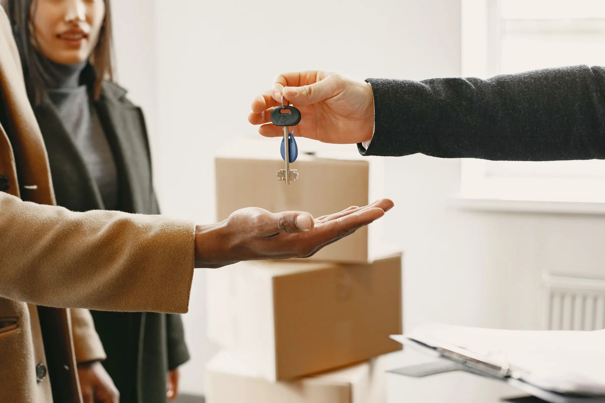 Iemand overhandigt huissleutels aan een nieuwe bewoner tussen verhuisdozen