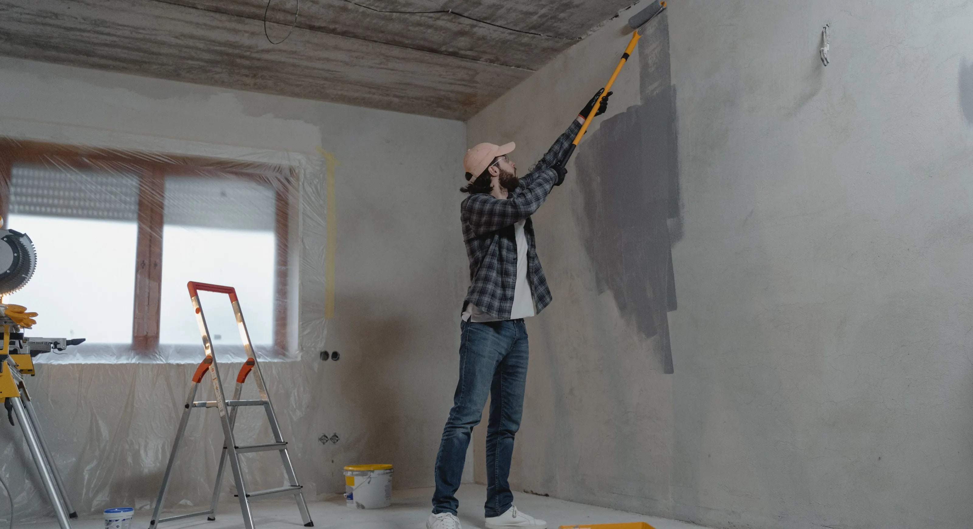 A painter rolling paint onto a wall with a roller on an extension pole