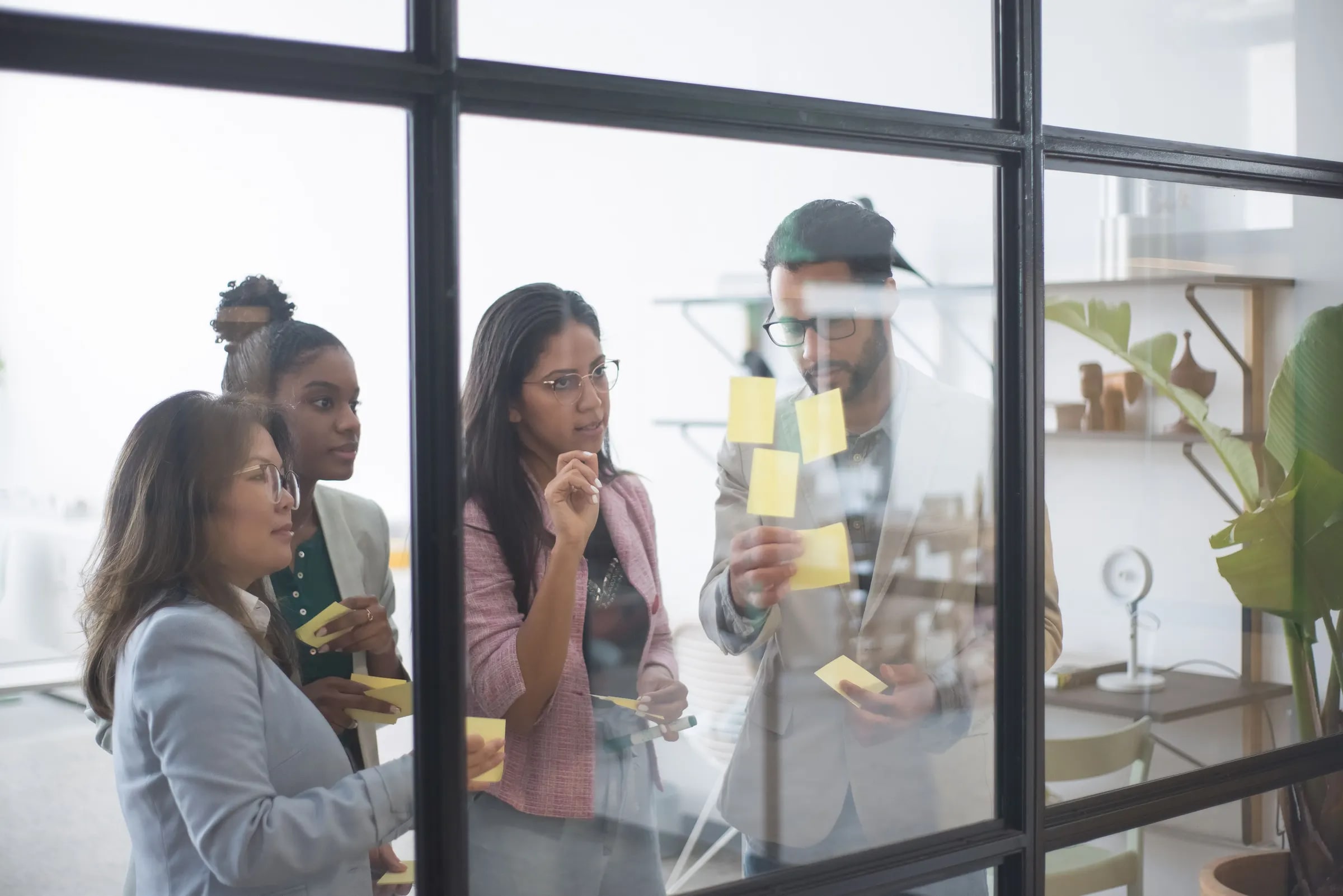 Four colleagues conferring at a glass wall covered in sticky notes