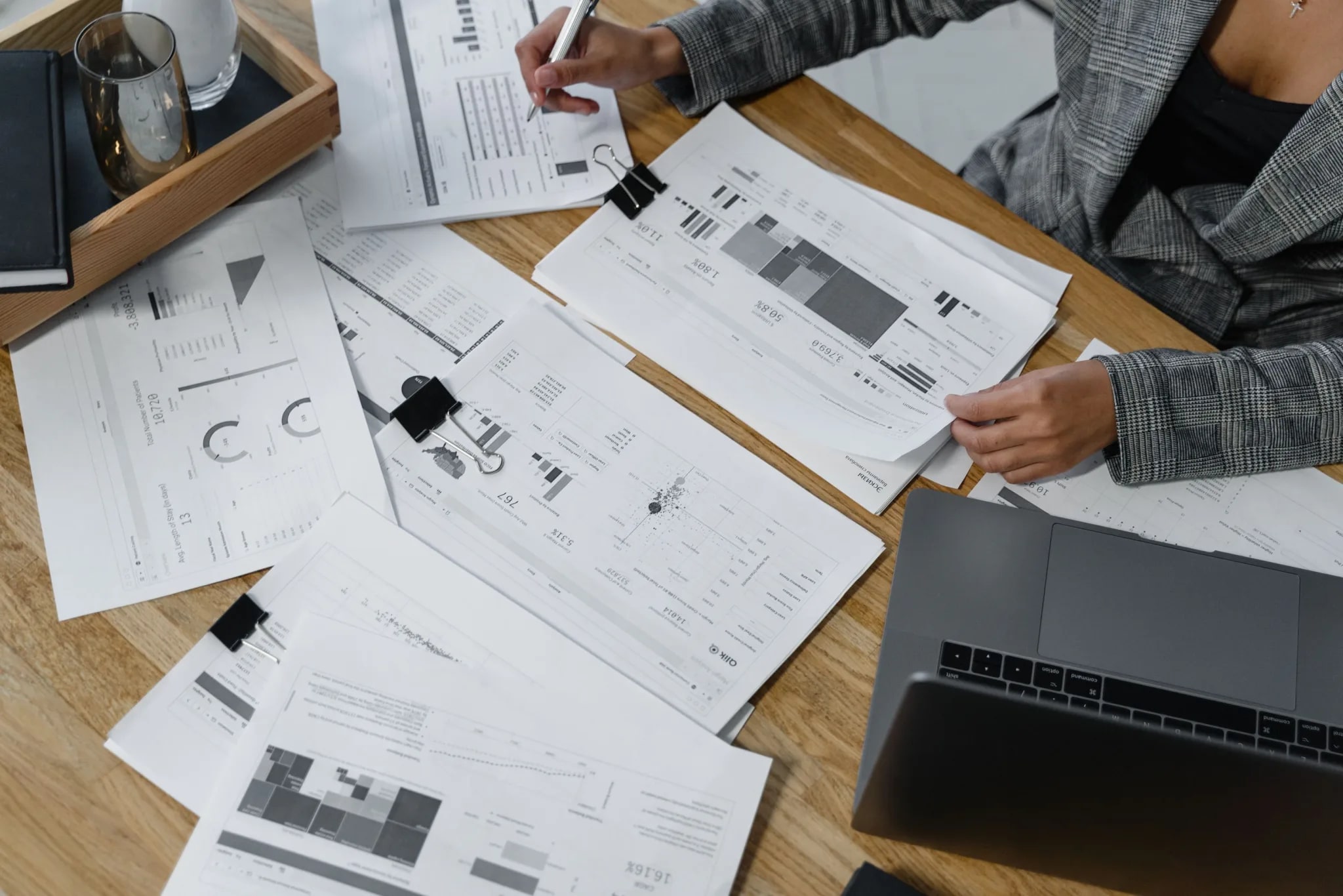 Handen met een pen boven financiële rapporten met grafieken, naast een laptop