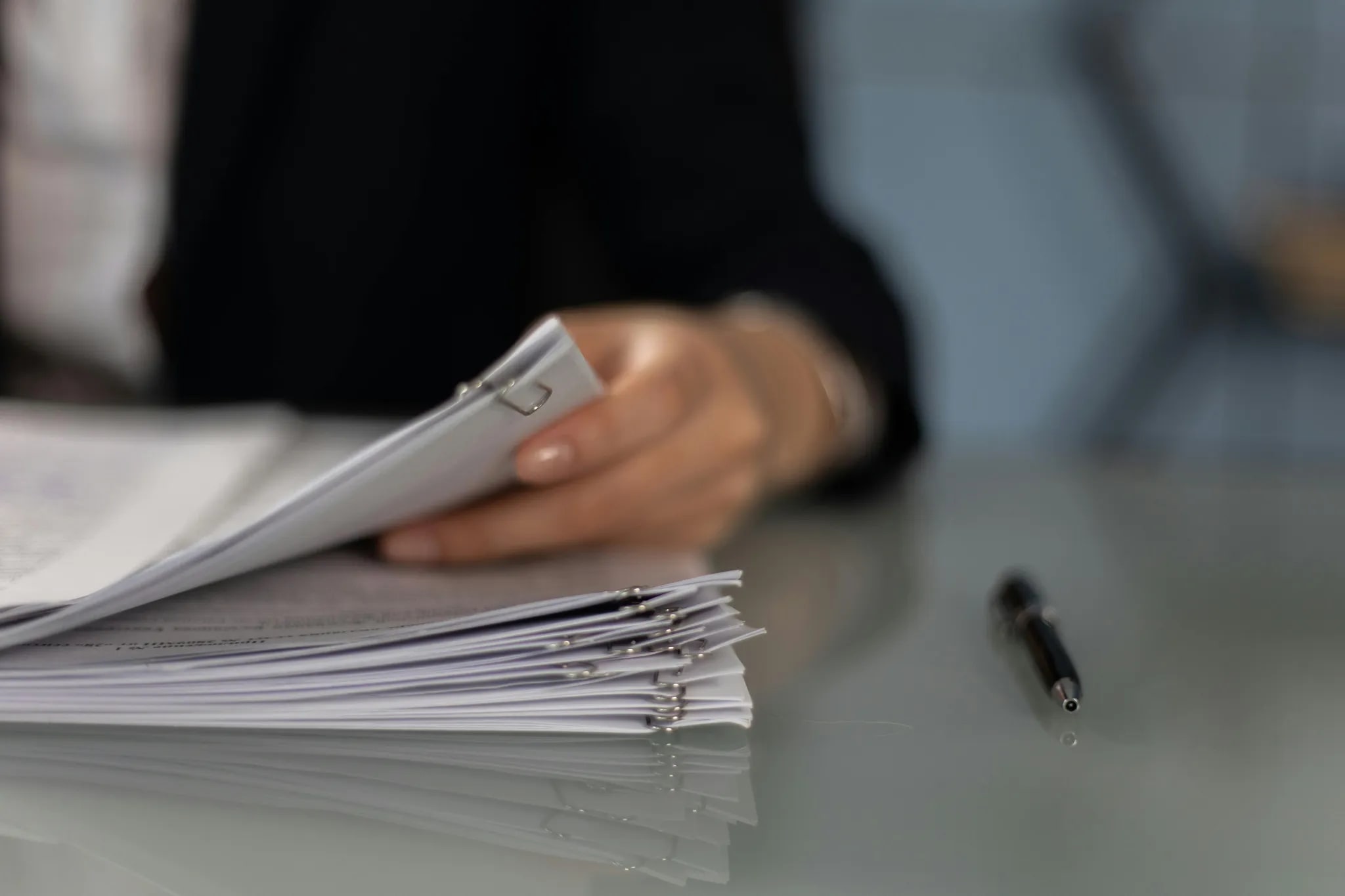 Een medewerker bladert door een stapel gebundelde documenten op een bureau