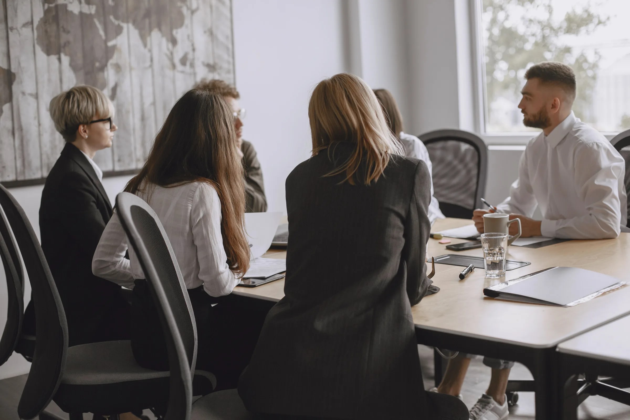 Een team zit in overleg rond een vergadertafel met laptops en documenten