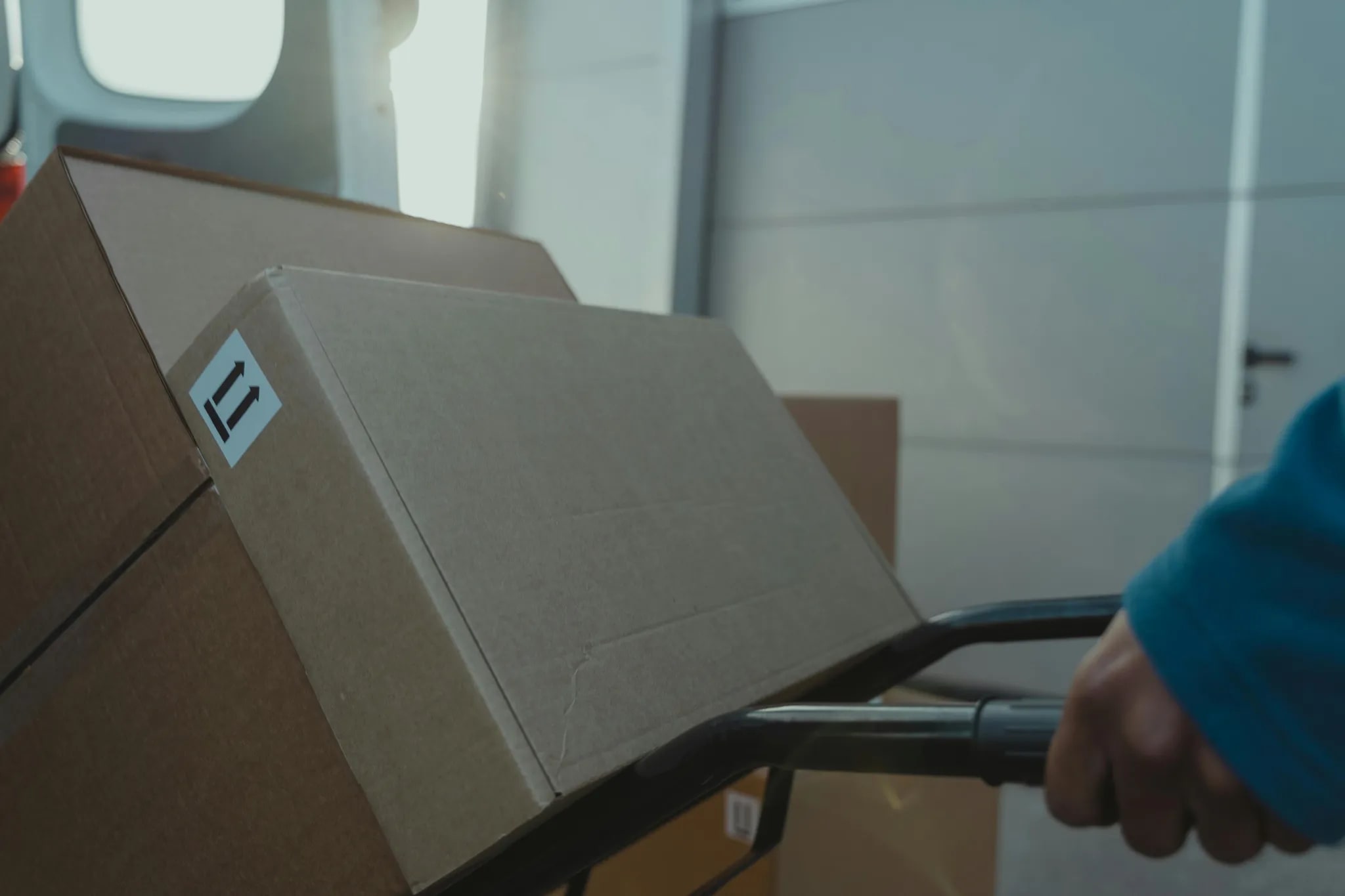 A courier wheeling a cardboard box on a hand truck into a delivery van