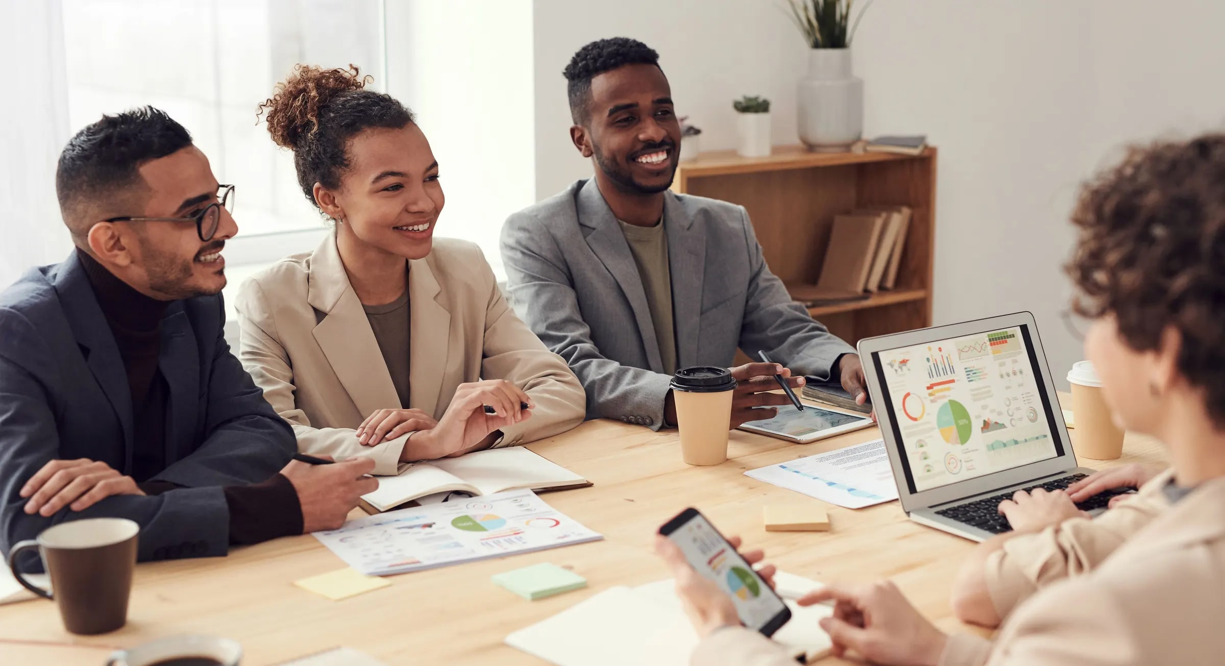 Een groep collega's zit lachend aan een vergadertafel met rapporten