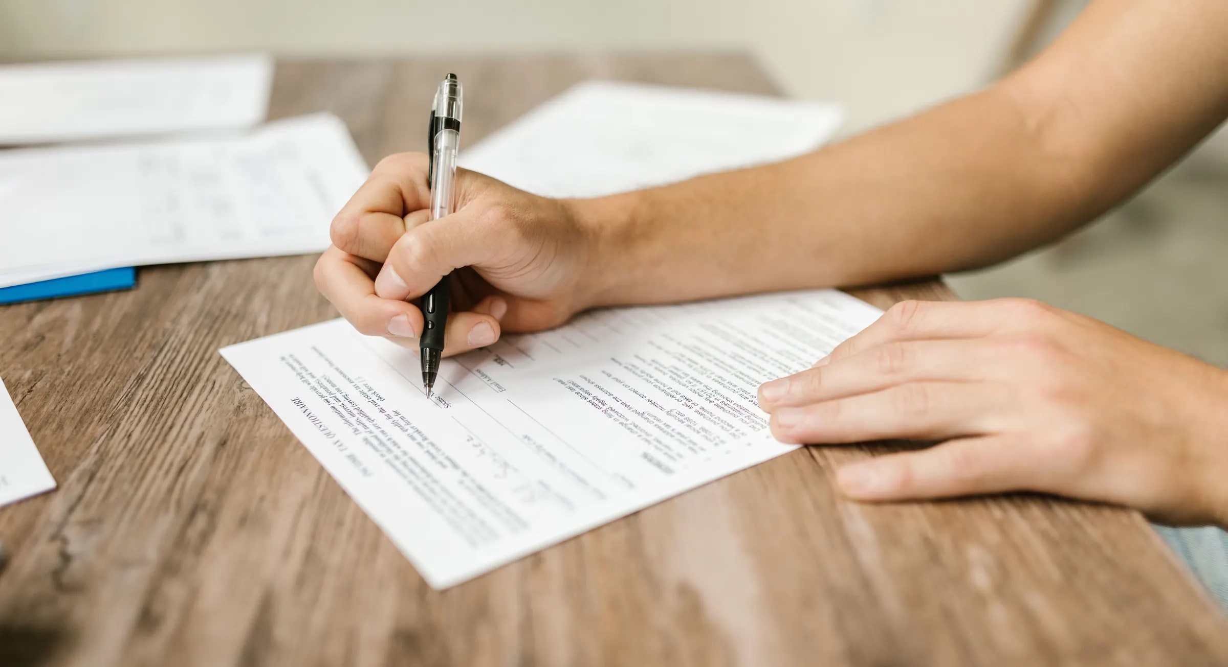 A hand filling in a paper form with a pen