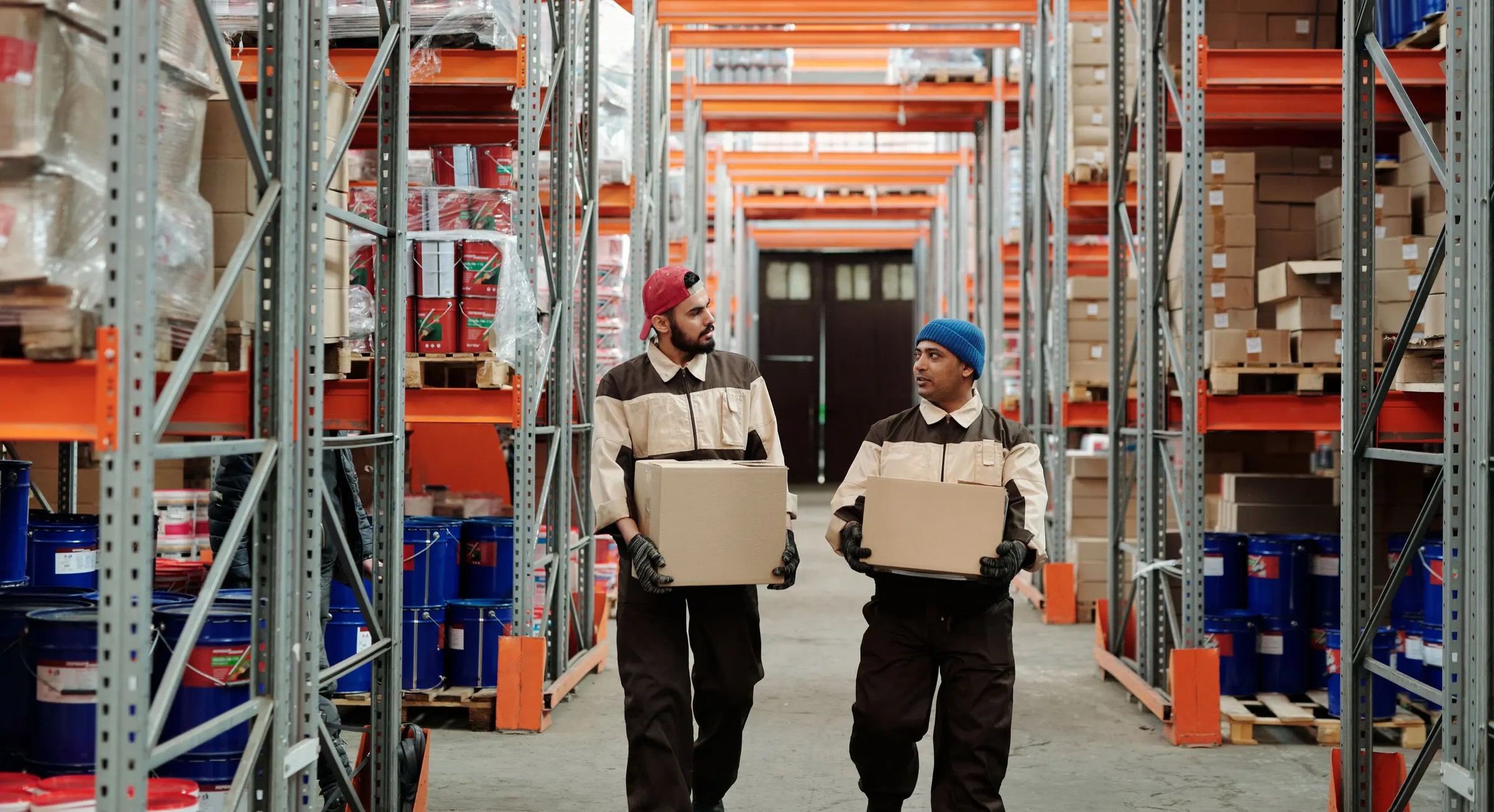 Two warehouse workers carrying boxes down an aisle of tall racking