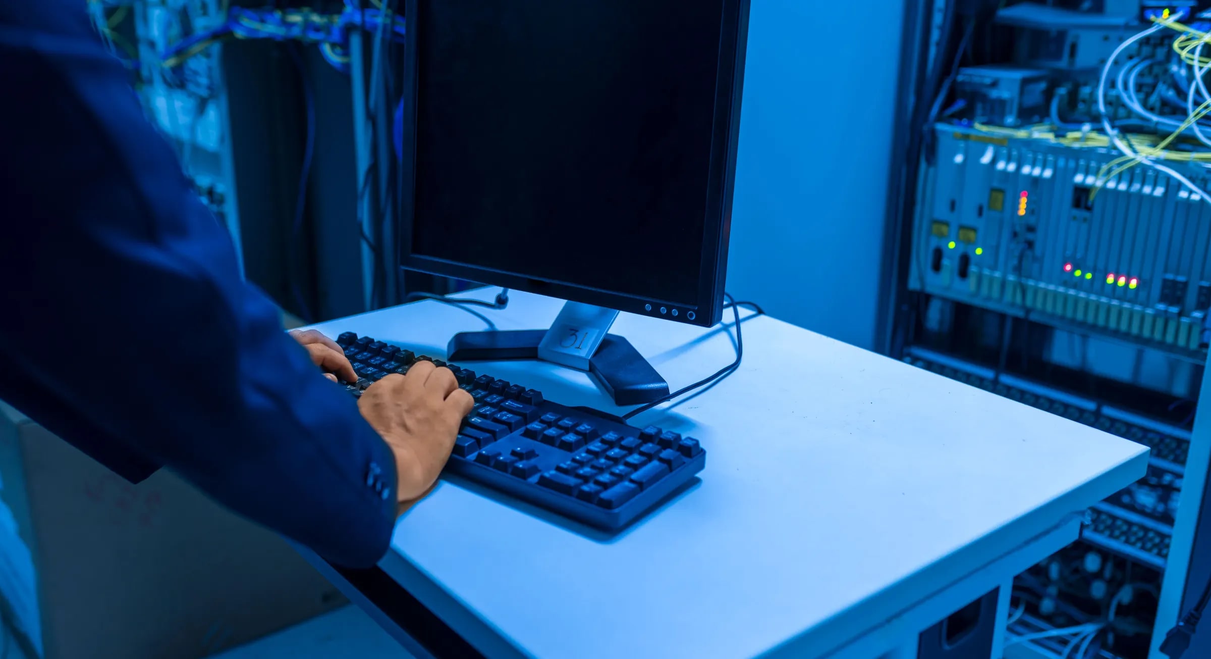 An administrator working at a monitor in a blue-lit server room