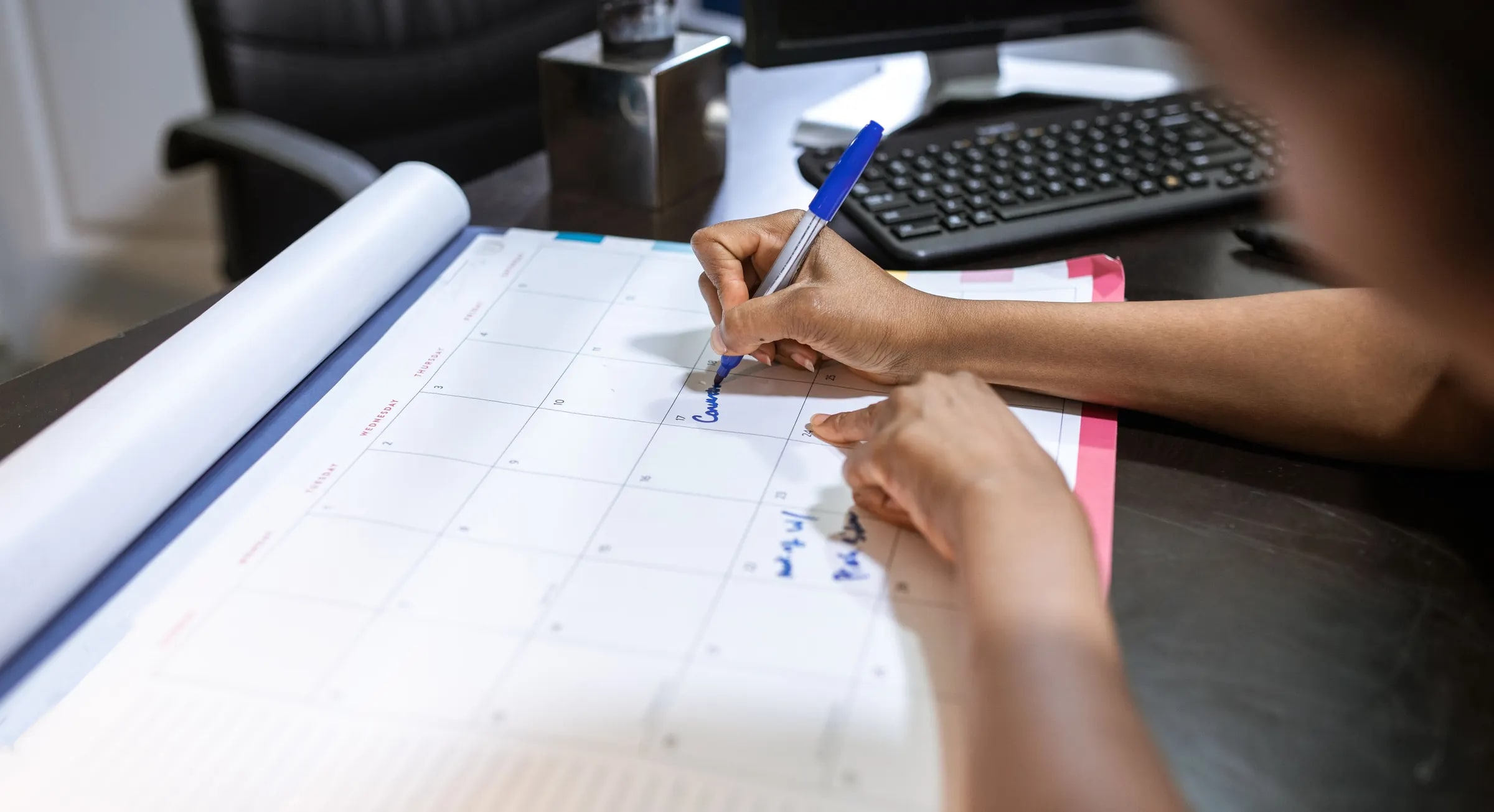 Hands filling in a schedule on a desk calendar