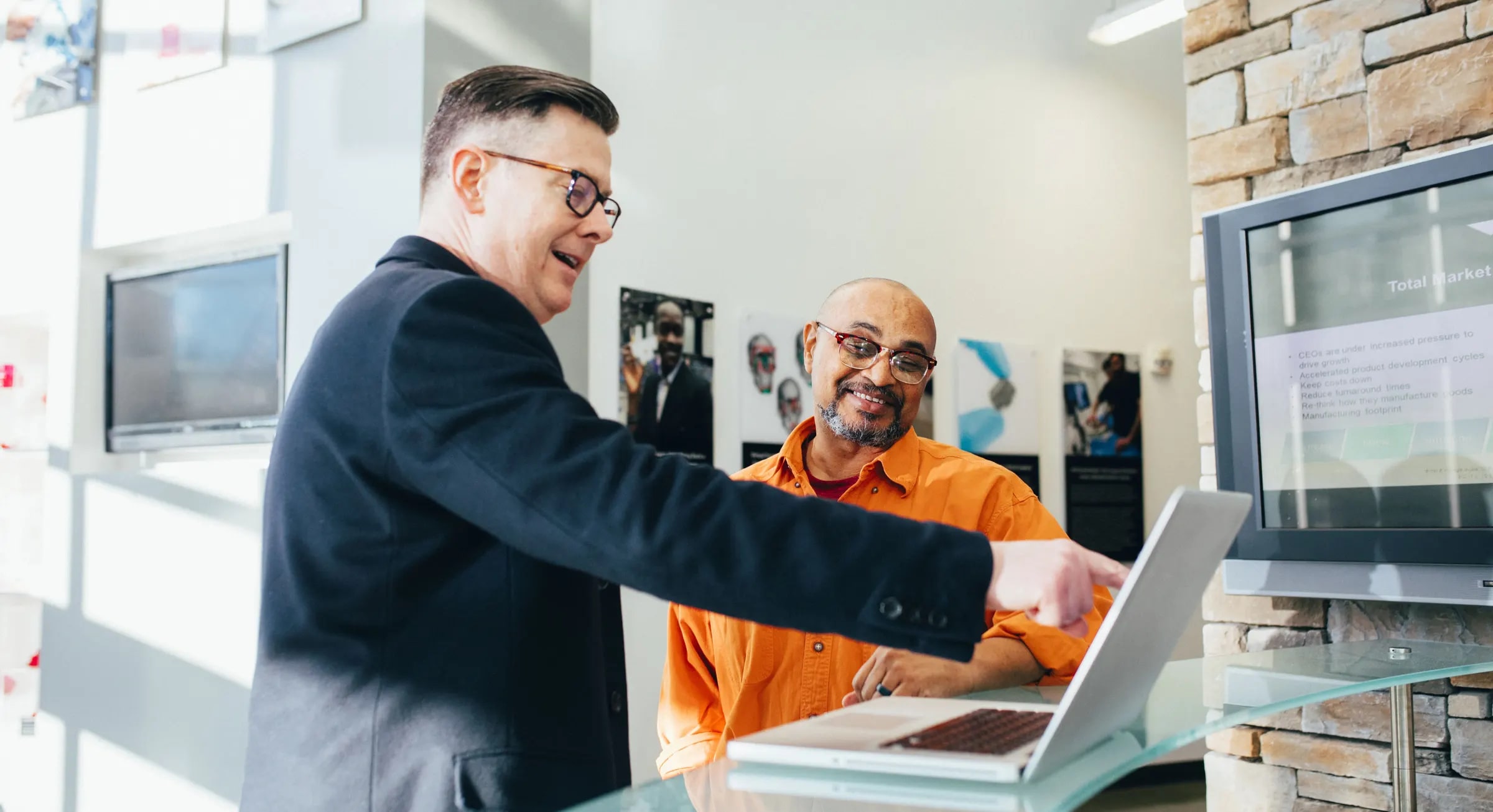 Two colleagues smiling and pointing at a laptop screen