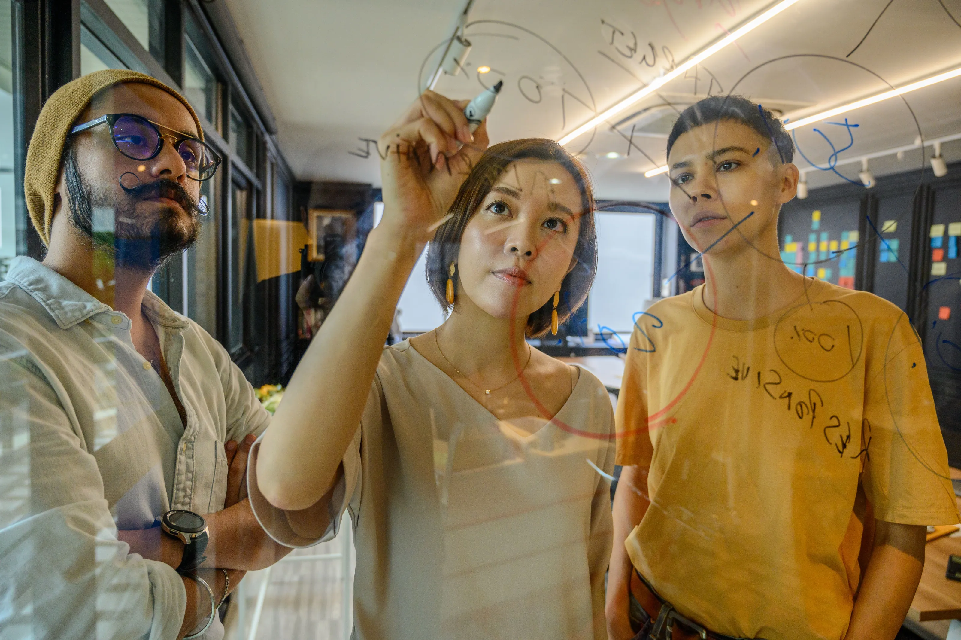 Drie collega's schetsen samen een idee op een glazen whiteboard