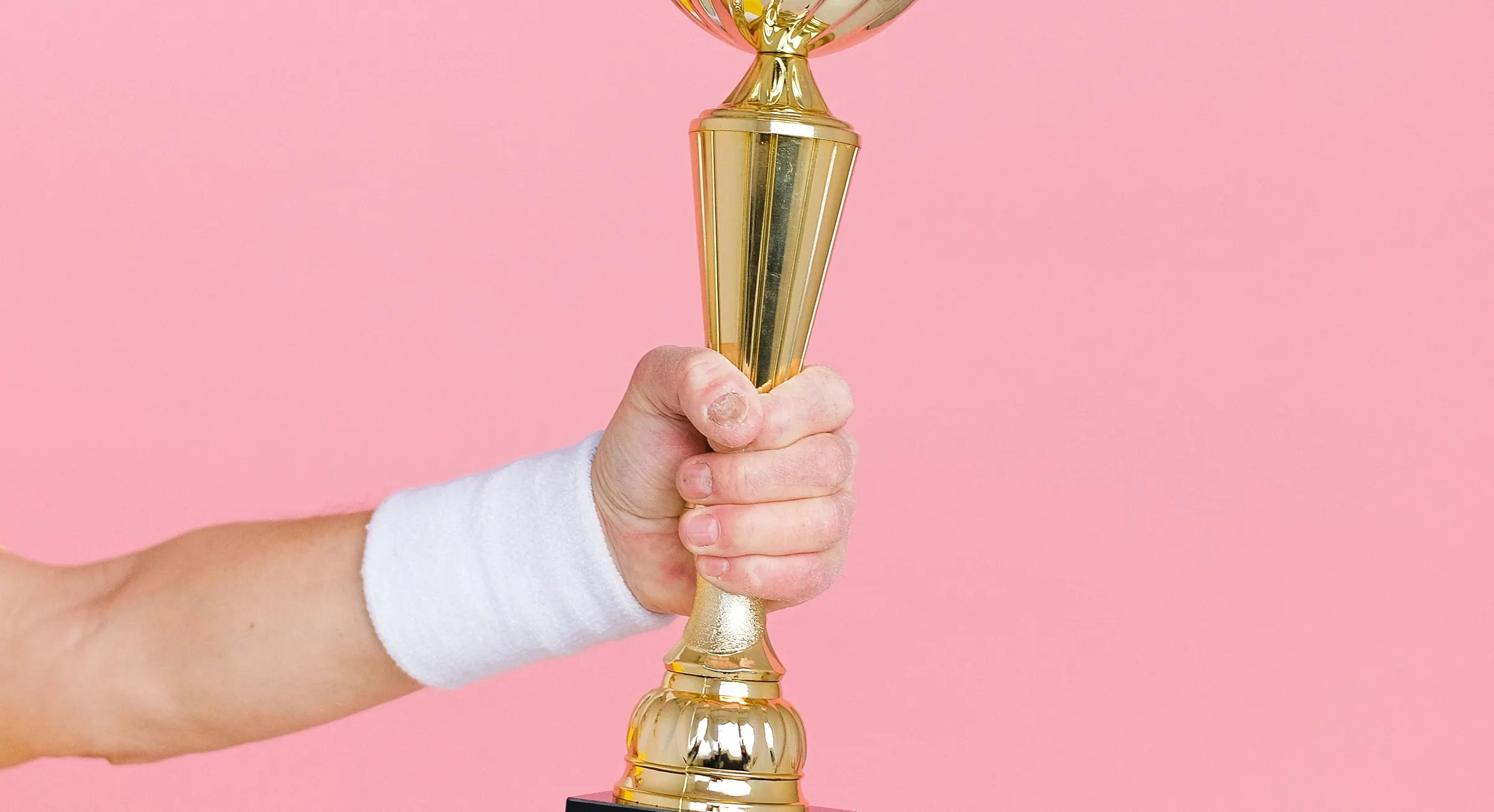 A hand holding up a golden trophy against a pink background