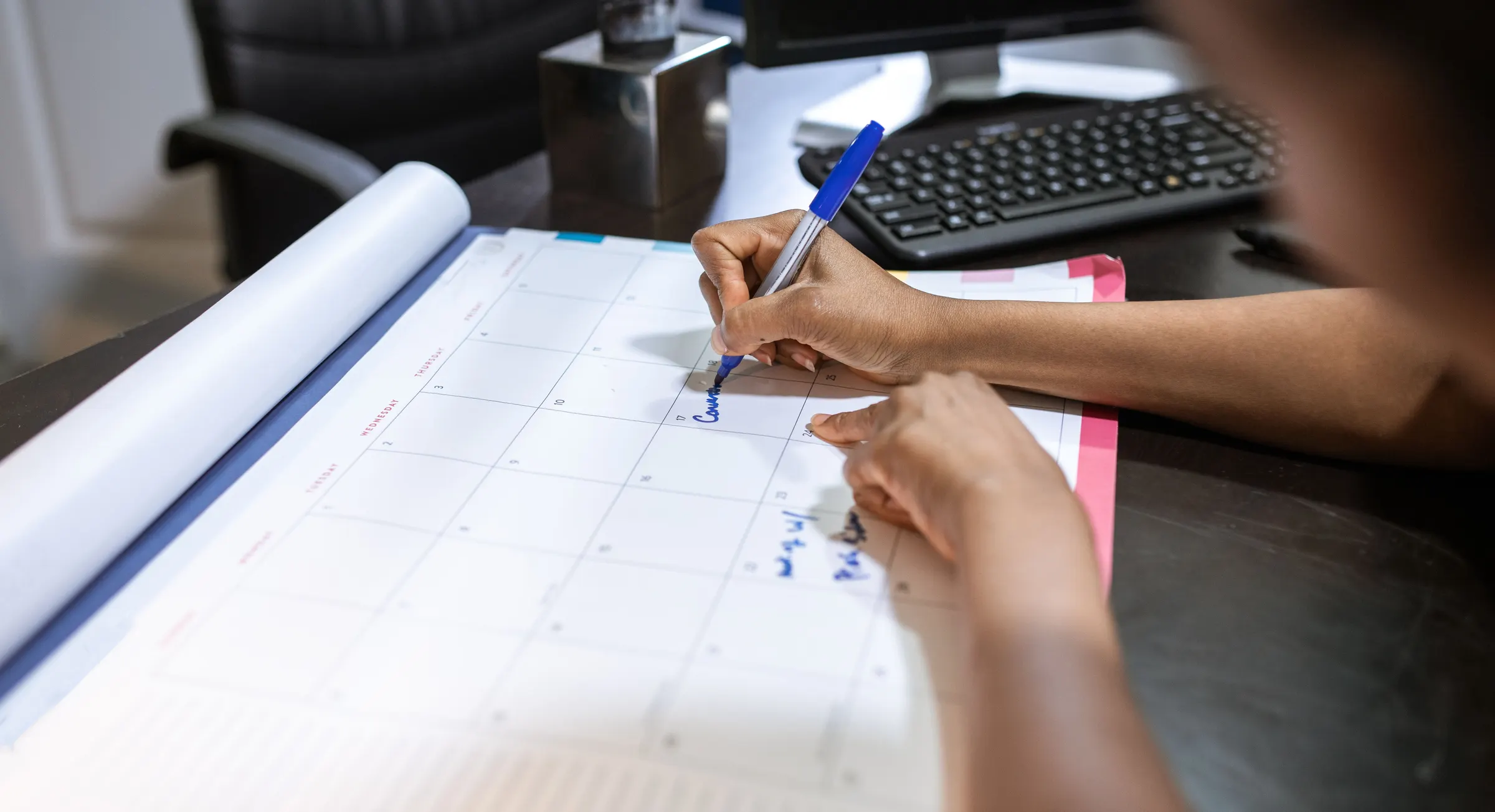 Hands filling in a schedule on a desk calendar