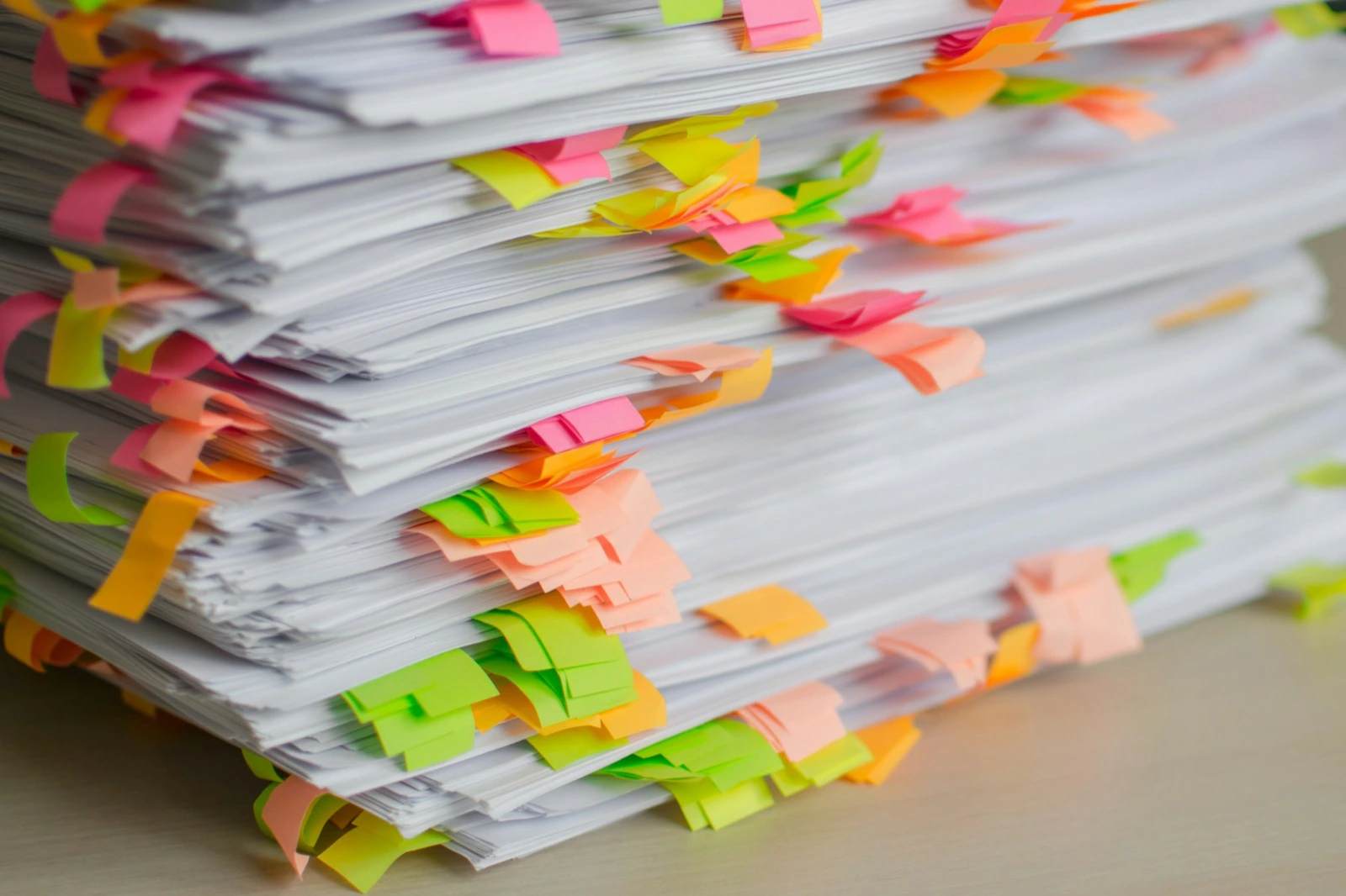 Een hoge stapel papieren vol gekleurde plaktabs op een bureau