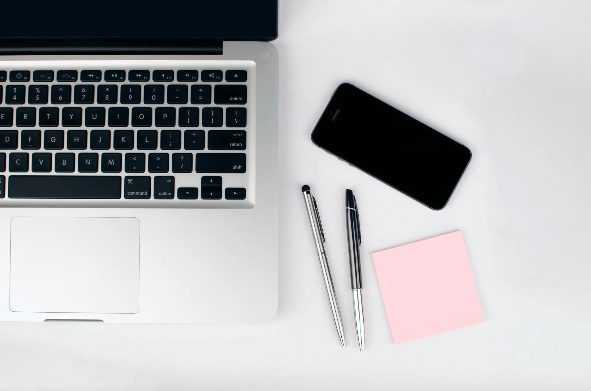 Laptop, smartphone, pens and a sticky note on a desk