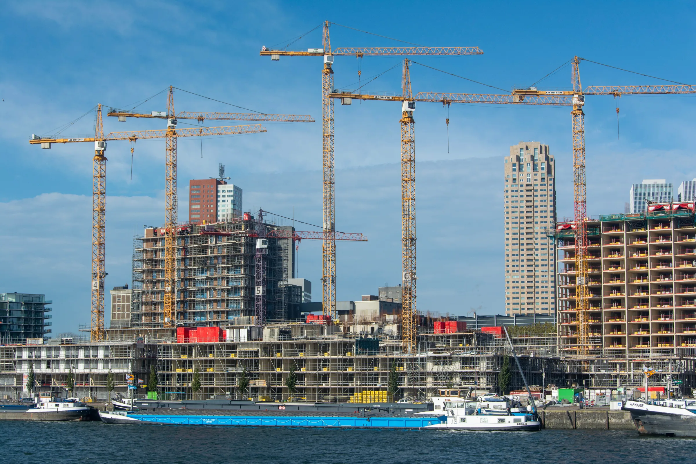Construction cranes above new buildings on the waterfront, with inland barges in the foreground