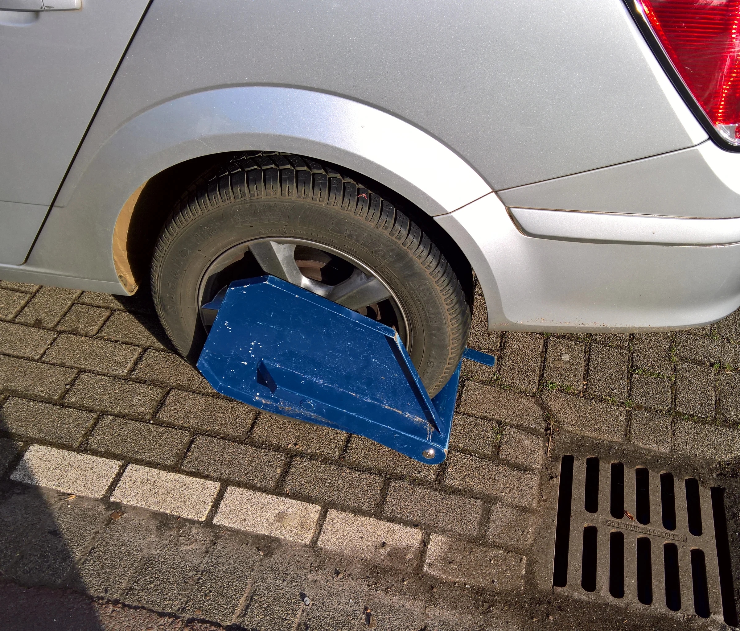 Een blauwe wielklem van de gemeente Rotterdam om het achterwiel van een geparkeerde auto
