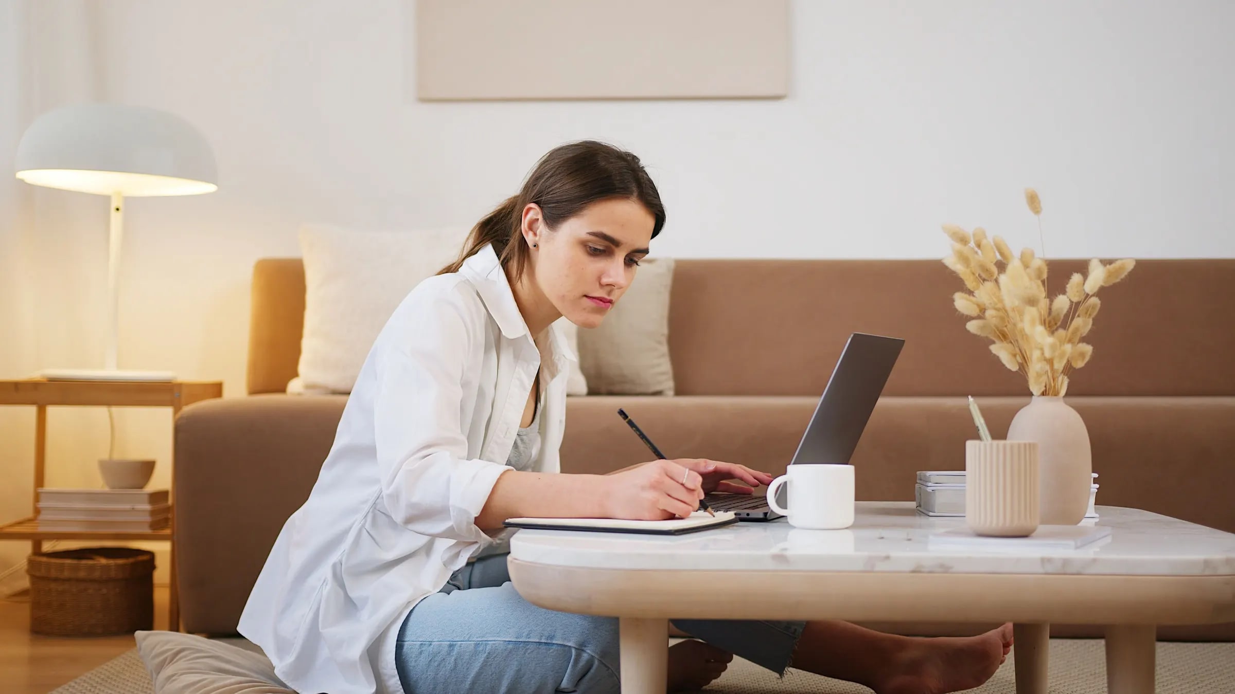 Een vrouw maakt aantekeningen bij een laptop in haar woonkamer