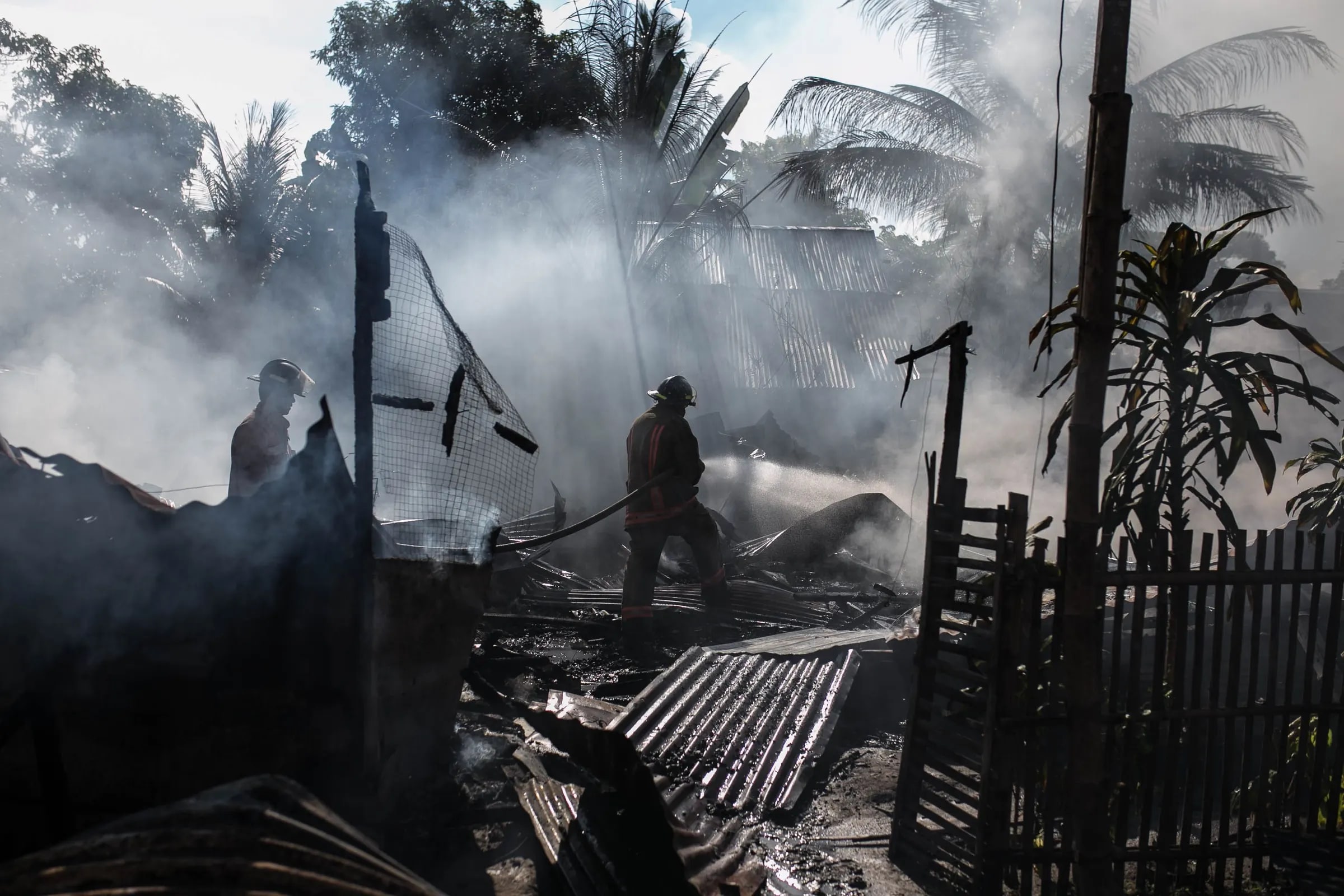 Brandweerlieden blussen een smeulende brand tussen de rook