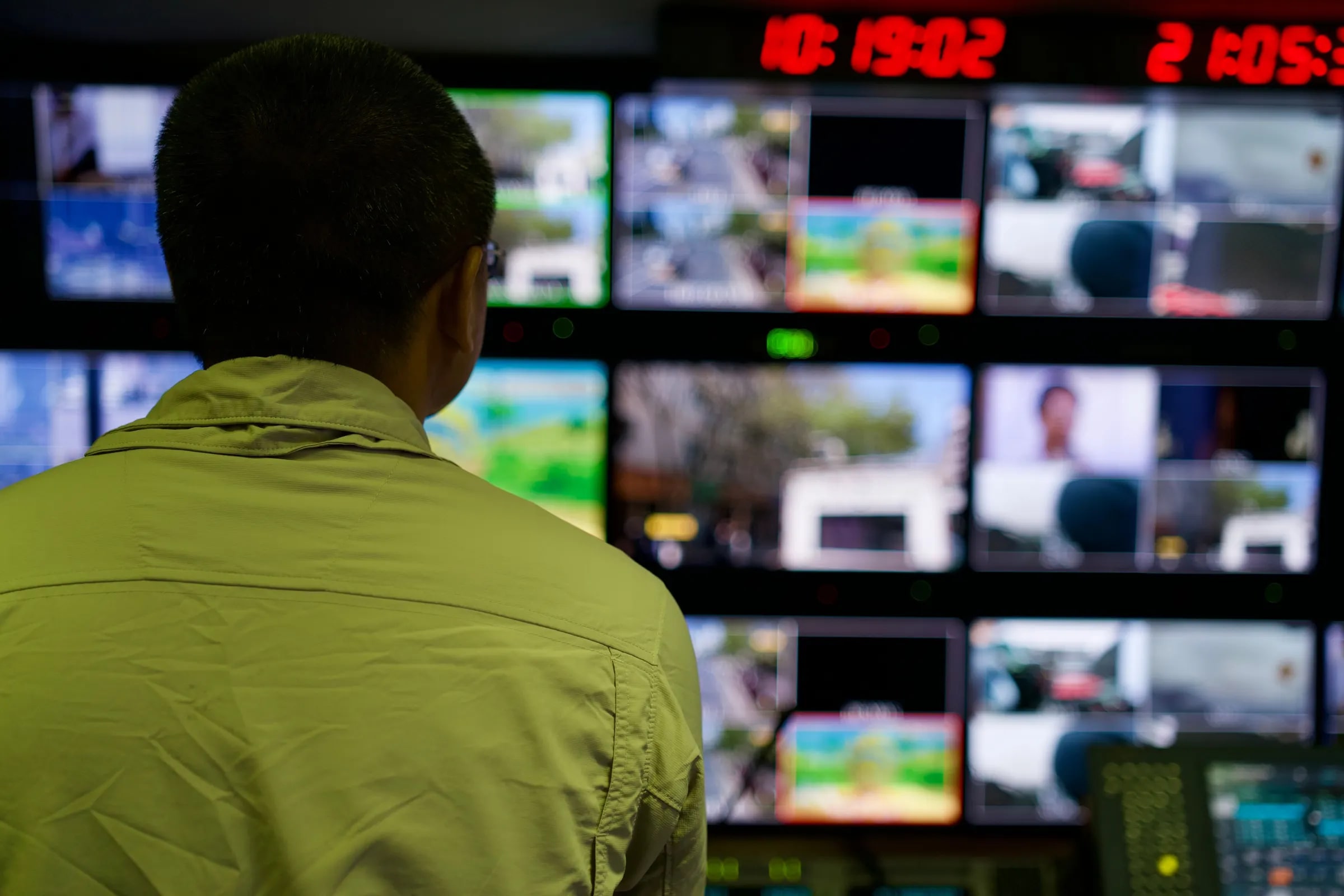 Een medewerker kijkt naar een wand vol beeldschermen in een controlekamer