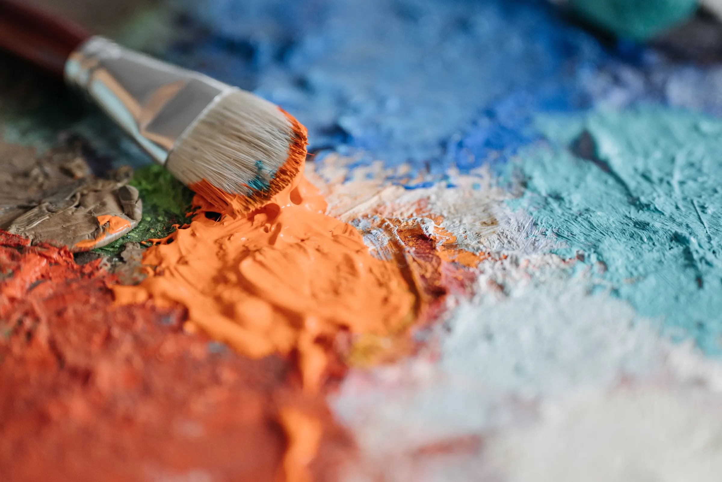 Een kwast naast dikke vegen oranje en blauwe verf