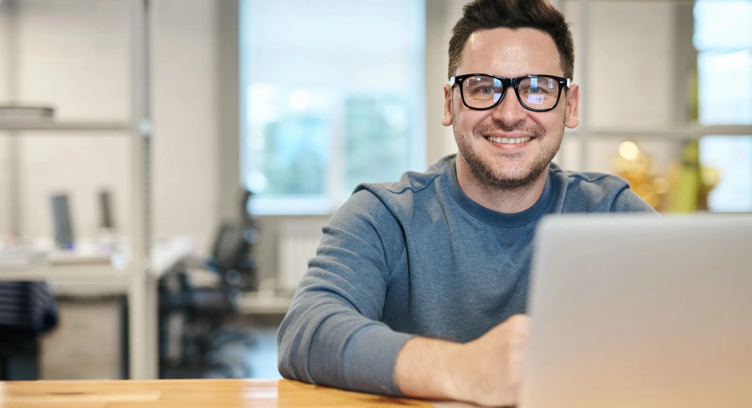 A smiling man working on a laptop in an office
