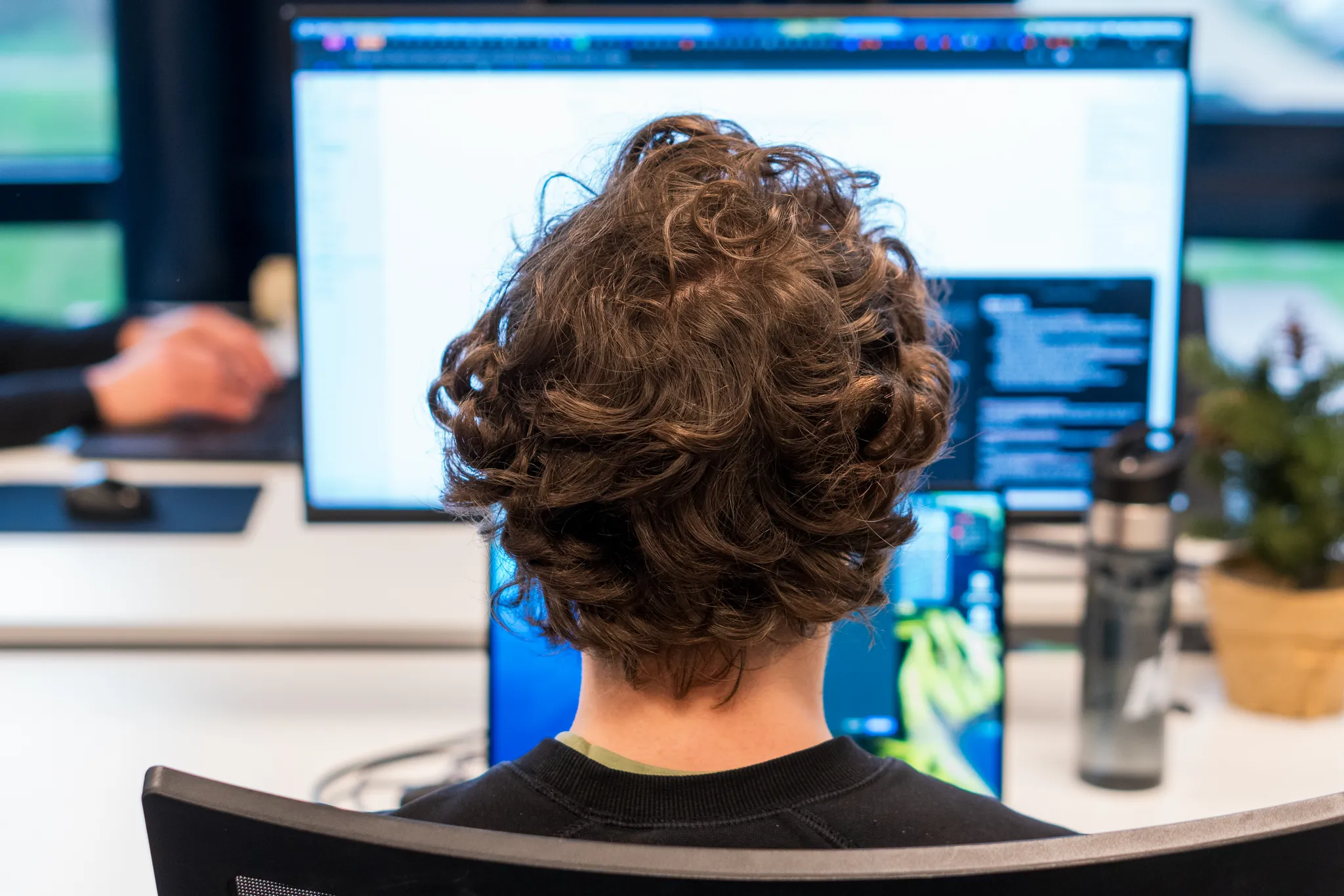 Een developer werkt geconcentreerd achter meerdere beeldschermen met code